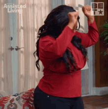 a woman in a red shirt is dancing in a living room with assisted living in the background