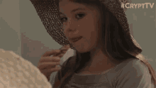 a young girl wearing a straw hat is eating a piece of food ..