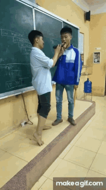two boys are singing into microphones in front of a blackboard with the words make a gif.com underneath them
