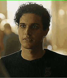 a young man with curly hair is wearing a black sweater with the letter s on it