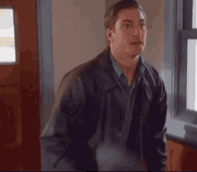 a man in a leather jacket is standing in front of a window in a hallway .