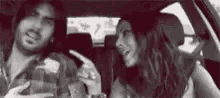 a man and a woman are sitting in the back seat of a car talking to each other .