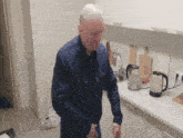 an elderly man in a blue shirt is standing in a kitchen