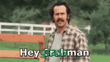 a man with a mustache is standing in front of a fence and says hey graslman