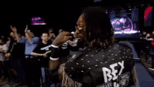 a man with dreadlocks wearing sunglasses is smiling in front of a crowd .
