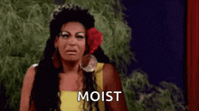 a woman with a flower in her hair is making a funny face and the word moist is on the screen .