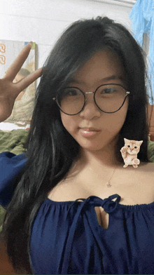 a woman wearing glasses is giving a peace sign with a cat on her shoulder