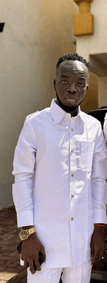 a man wearing a white shirt and white pants holds a cell phone