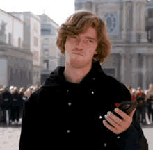 a man in a black jacket holds a cell phone in his right hand