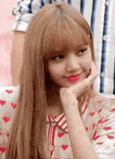 a close up of a woman with long blonde hair and bangs holding her hand to her chin .