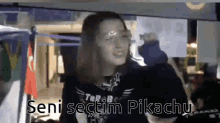 a girl in a black shirt is holding a sign that says seni sectim pikachu