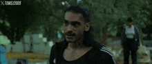 a man with long hair and a mustache is standing in front of a sign that says xtoms1205
