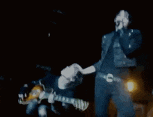 a man is playing a guitar and singing into a microphone while another man holds a guitar .