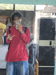a man in a red shirt is taking a picture of himself in front of a sign that says " alt "