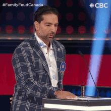 a man in a plaid suit stands in front of a microphone with the hashtag familyfeudcanada