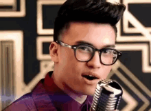 a young man wearing glasses is singing into a vintage microphone