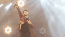 a man is singing into a microphone on a stage with his hands in the air .