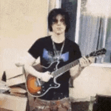 a man is playing a guitar in front of a window in a living room .