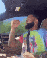 a man in a tie dye shirt and tie is driving a car