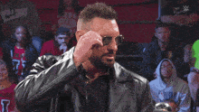 a man wearing a leather jacket holds a pair of glasses in his mouth