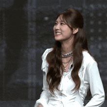 a woman wearing a white shirt and necklace smiles