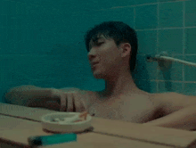 a shirtless man is taking a bath in a bathtub with a cigarette in the ashtray .