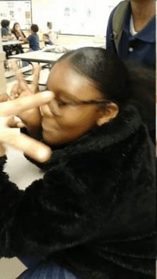 a young girl wearing glasses is sitting at a table in a classroom .