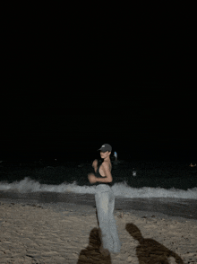 a woman is standing on a beach at night wearing a black hat