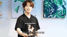 a young man wearing a black t-shirt with a cat on it is standing in front of a wall .