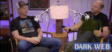 two men are sitting in chairs talking to each other in front of microphones .