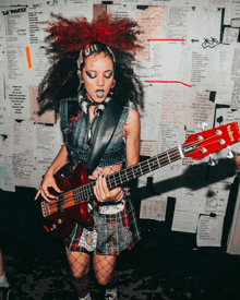 a woman playing a bass guitar in front of a wall with papers on it that say la plaza