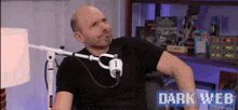 a bald man is sitting in front of a microphone with the words dark web behind him