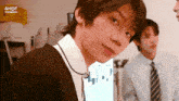 a boy in a suit and tie is looking at the camera while another boy looks on .