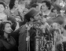 a man stands in front of a microphone with progress on his back