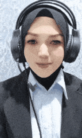 a woman wearing headphones and a hijab is smiling .