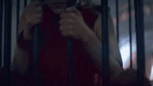a man in a red shirt is behind bars in a jail cell