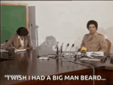 two men are sitting at a table with microphones and one of them is saying " i wish i had a big man beard "
