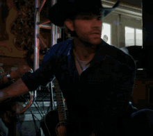 a man wearing a cowboy hat is holding a guitar
