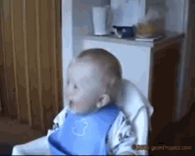 a baby is sitting in a high chair wearing a blue bib with a bottle on it