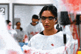 a woman in a lab coat and goggles is holding a bloody object in front of a sign that says 2