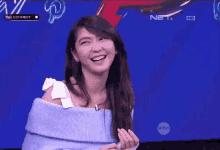 a woman in a blue sweater is laughing in front of a blue screen .