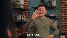 a man in a green sweater says " happy tears " in front of a brick wall