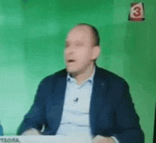a man in a suit is sitting in front of a green screen with a number 3 on it .