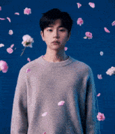 a young man in a grey sweater is surrounded by pink flowers on a blue background