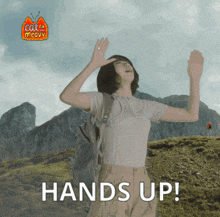 a woman with a backpack is standing in front of a mountain and says hands up
