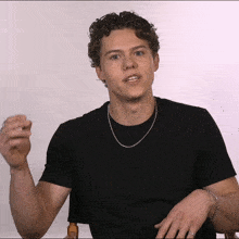 a young man with curly hair wearing a black shirt and silver chain