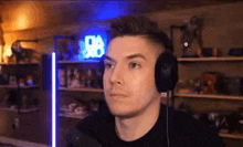a man wearing headphones is looking at the camera in a room with a neon sign in the background .