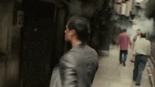 a man in a leather jacket is walking down a narrow alleyway with other people .