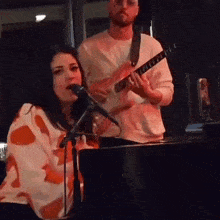 a woman is singing into a microphone while a man is playing a guitar .