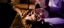 a person is laying on a couch with their hands on their face and a purple light behind them .
